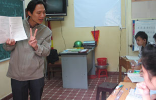 Thầy Phúc dạy toán đang giảng bài bằng tay và sách giáo khoa.