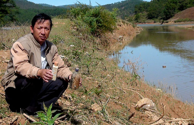 Ông Nguyễn Văn Dũng nhặt lên những chai thuốc sâu còn vướng lại bên bờ suối.