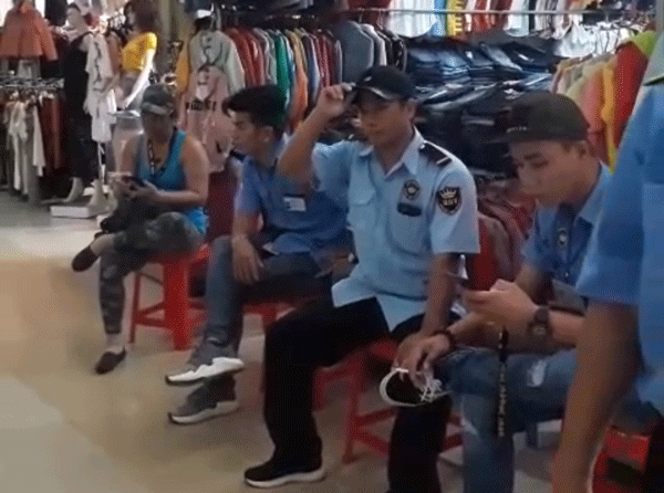 Nhóm người "đòi nợ thuê" ngồi dàn hàng ngang trước một cửa hàng quần áo tại chợ Bảo Lộc để buộc tiểu thương nộp tiền 