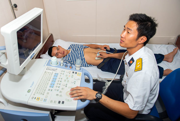 Phòng Siêu âm là nơi các y - bác sĩ của tàu có thể hội chẩn trực tuyến với đồng nghiệp ở Bệnh viện Quân y 175 (TP Hồ Chí Minh) qua vệ tinh Vinasat. Ngoài máy siêu âm 4 màu, tàu còn được trang bị nhiều thiết bị y tế hiện đại như: máy thở, máy sốc tim, máy tạo ôxy, máy rửa dạ dày tự động, hệ thống monitor theo dõi bệnh nhân. Trong ảnh: Trung úy Nguyễn Thanh Tùng (Y sĩ của tàu) đang siêu âm cho 1 chiến sĩ bị đau bụng.
